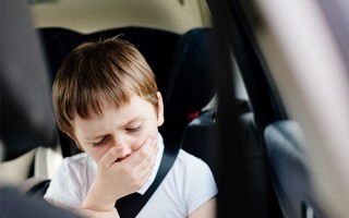 Ein kleiner junge hält sich die Hand vor dem Mund im Auto.