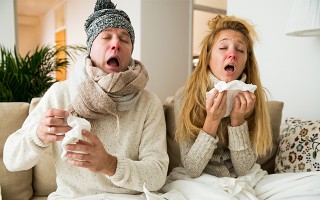 Zwei erkältete Personen niesen auf dem Sofa