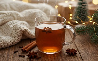 Dampfende Tasse Tee mit Sternanis und Zimt auf Holztisch, umgeben von winterlicher Deko