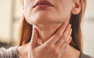 Frau berührt ihren Hals im Bereich der Schilddrüse.