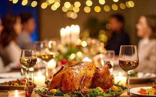 Festlicher Tisch mit gebratenem Truthahn, Kerzen und Wein, Menschen sitzen unscharf im Hintergrund.