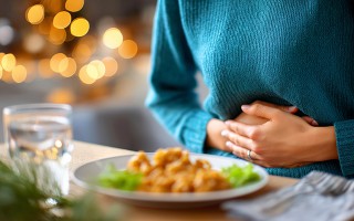 Person hält sich den Bauch vor einem Teller Essen, als Hinweis auf Unwohlsein oder Bauchschmerzen.