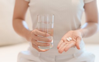 Frau hält Tabletten und ein Wasserglas.