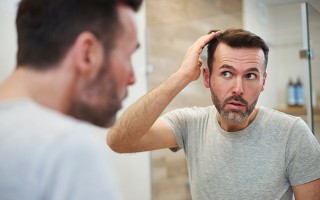 Mann betrachtet besorgt seinen Haaransatz im Badezimmerspiegel.