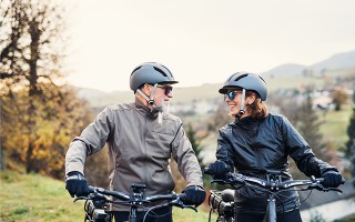 Älteres Paar fährt gemeinsam E-Bike in der Natur.