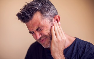 Mann hält sich mit schmerzverzerrtem Gesicht das rechte Ohr, vermutlich wegen starker Ohrenschmerzen.