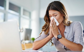 Frau schnäuzt sich am Arbeitsplatz