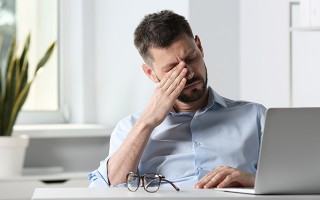 Mann reibt sich muede die Augen am Schreibtisch.