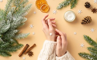 Person trägt Handcreme auf, umgeben von winterlicher Deko wie Tannenzweigen, Zimt und getrockneten Orangenscheiben.