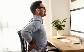 Mann mit Rückenschmerzen am Schreibtisch