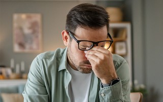 Mann reibt sich erschöpft die Augen am Tisch sitzend.